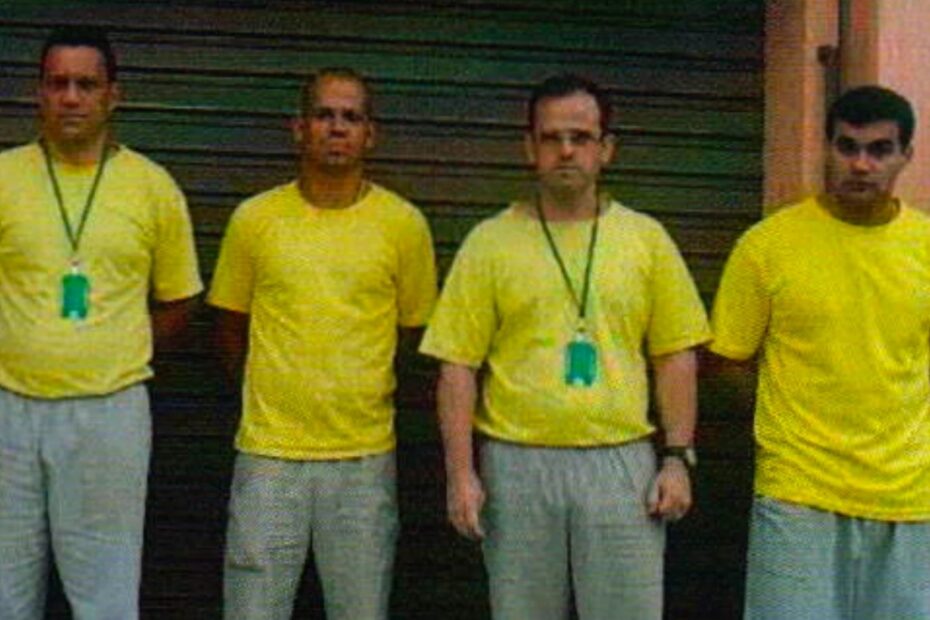 Os policiais militares Carlos Magno dos Santos Diniz, Márcio Barra da Rocha, Ricardo José Manso Monteiro e Alex Sandro Soares Machado, de camiseta amarela, lado a lado diante de uma porta de aço, em 2012