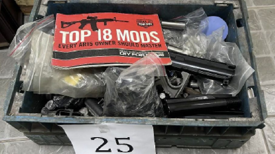 Caixa com componentes de fuzil AR-15 apreendidos pela Polícia Federal contendo manual técnico "TOP 18 MODS - Every AR15 Owner Should Master", indicativo de operação sofisticada de customização e modificação de armas.